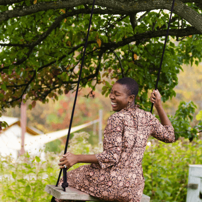 Guest swinging on tree rope seat and smiling with vibrant green autumn foliage at La Tourelle Hotel and Sp