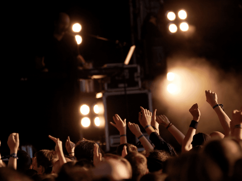 Concert crowd cheering with raised hands under stage lights