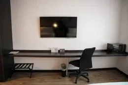 Wall-mounted flat-screen television above long, minimalist, dark work desk with rolling black office chair at Unika Hotels