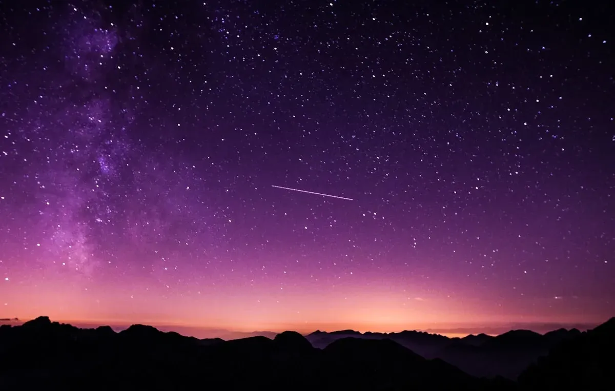A star-filled night sky glowing purple over dark mountain ridges