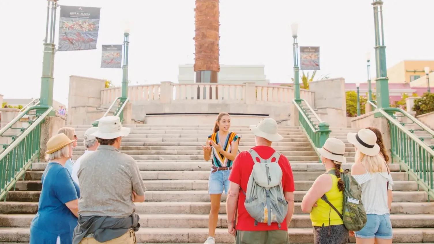 Tour group with guide standing before historic brick tower monument with wide stone staircase and green railings.
