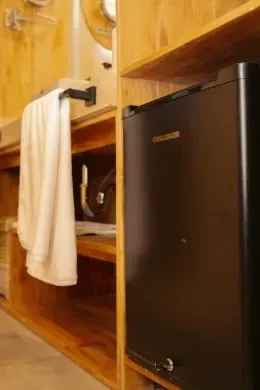 Black mini fridge set beside a wood-slat cabinet, with a folded towel hanging under a wall towel rail at Unika Hotels