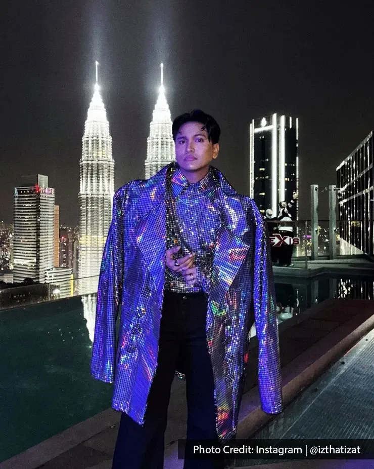 A man poses in glittering attire with the illuminated Petronas Twin Towers in the background.