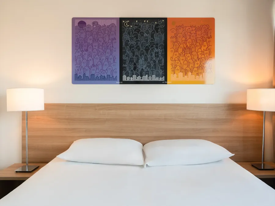 Two-bedroom apartment with a large bed and modern artwork at Appart’Hôtel Hévéa in Valence.