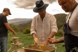 Chef wearing a fedora hat kneading ground corn dough in a metal tray during an outdoor culinary workshop at Unika Hotels
