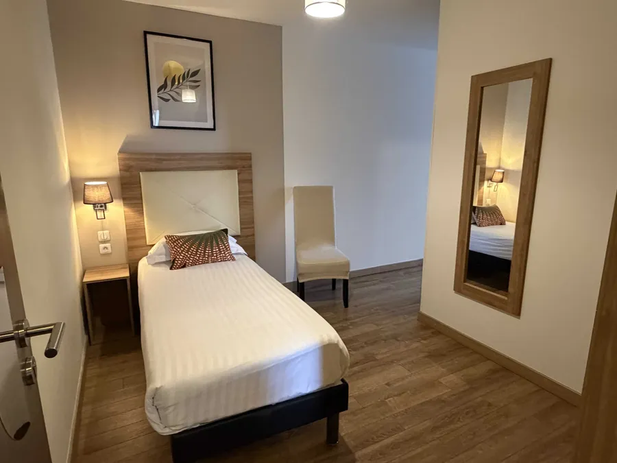 Chambre triple avec lit, chaise et miroir au Le Grand Hôtel Molière à Pézenas.