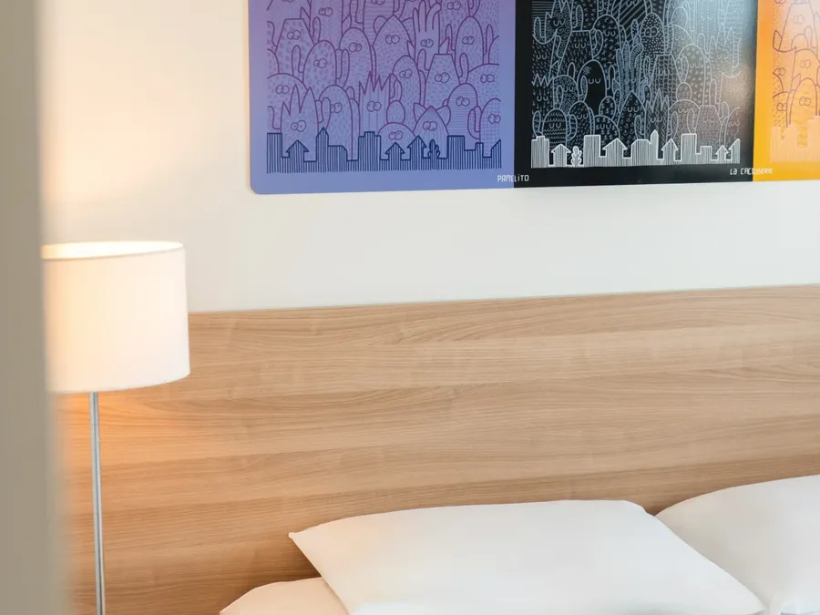 Two-bedroom apartment at Appart’Hôtel Hévéa in Valence with a bed, nightstand, and lamp.