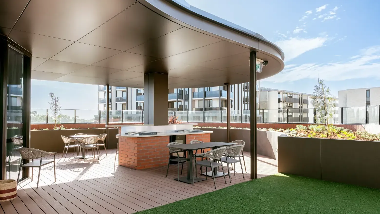 Outdoor rooftop lounge area with wooden flooring, green turf, and modern furniture at Caulfield Place.