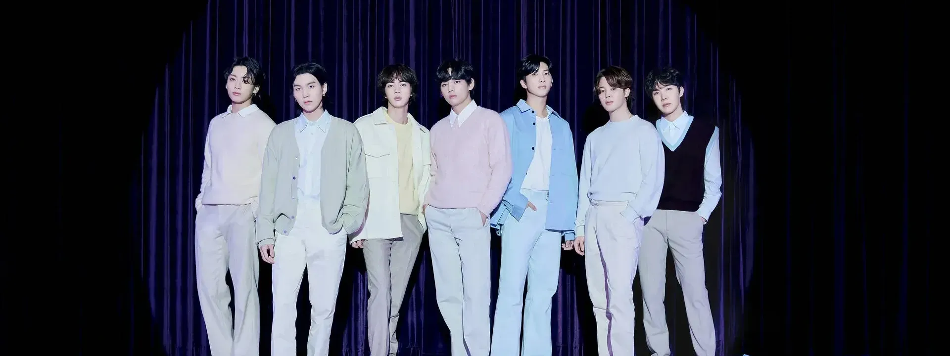 BTS performing live on stage with dynamic lighting and an enthusiastic crowd at a concert.