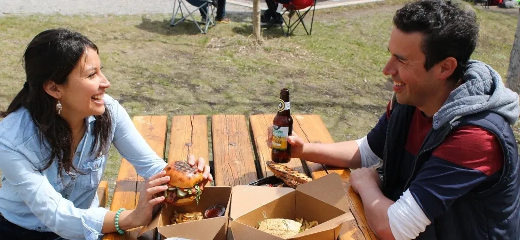 A couple share food and drinks at a picnic table in a walkable park in Canmore.