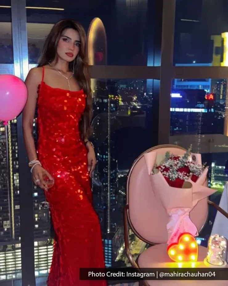 A woman in red sparkling dress posing for a romantic dinner photo with city views.