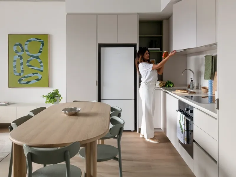 Woman reaching for a bowl in a modern kitchen with white cabinets and wooden table.