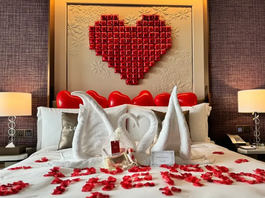 Romantic setup with swan towels and red petals on bed under a heart-shaped decor showcasing the Forever Yours Package.