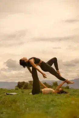 Two people practicing acro yoga on a grassy hill beneath a cloudy sky at Unika Hotels, one of the best hotels in Bogota