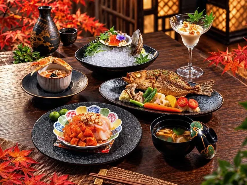 Hokkaido Harvest Kaiseki featuring grilled fish, fresh oyster on ice, sashimi, soup, and dessert on wooden table with autumn leaves.