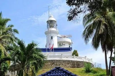 A white lighthouse atop a hill surrounded by palm trees against a clear blue sky - Lexis Hibiscus Port Dickson