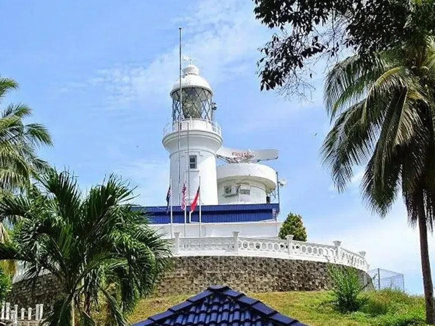 A white lighthouse atop a hill surrounded by palm trees against a clear blue sky - Lexis Port Dickson