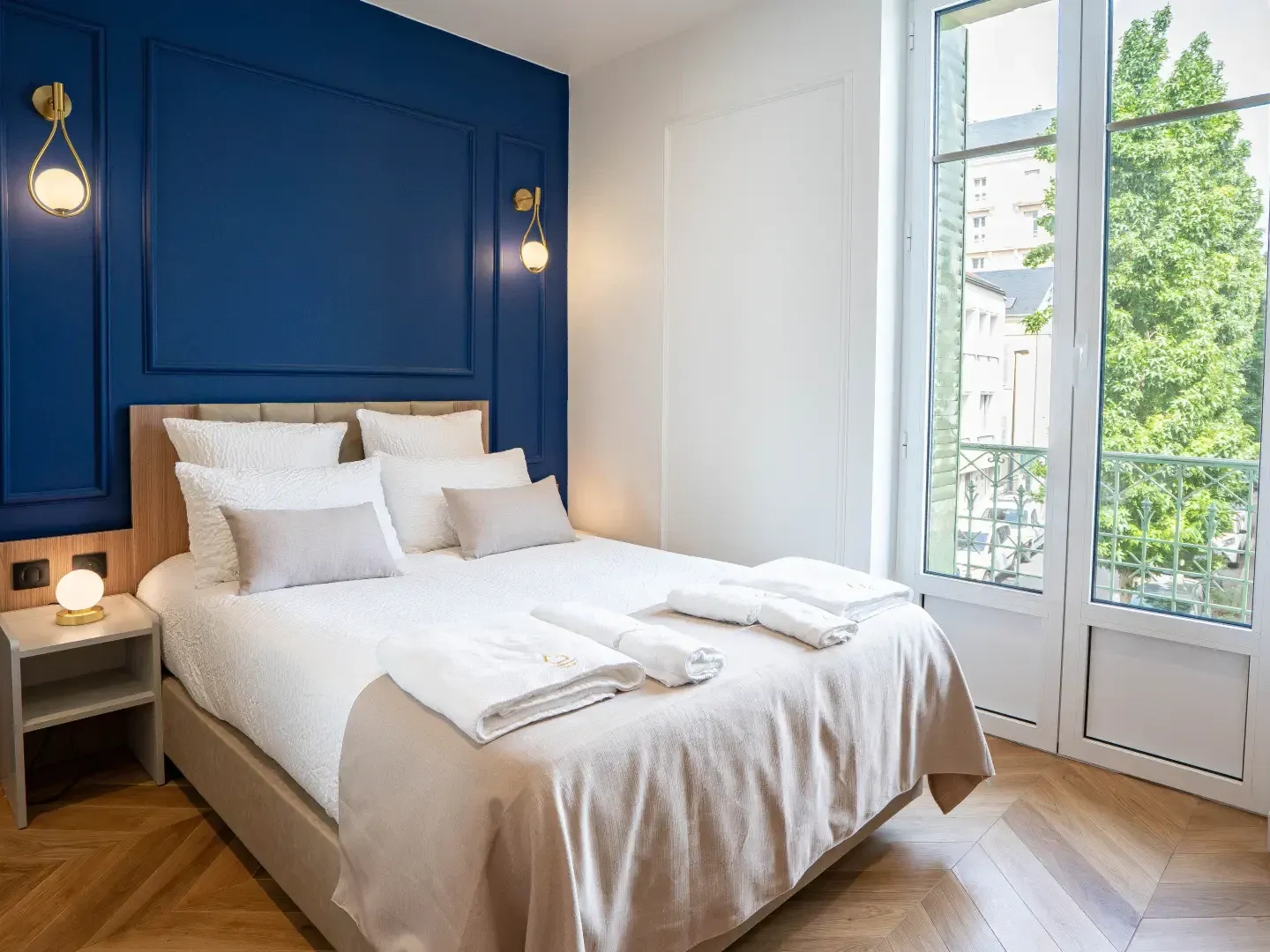 Chambre lumineuse avec lit double, mur bleu marine et grandes fenêtres donnant sur la verdure aux Sources Callou