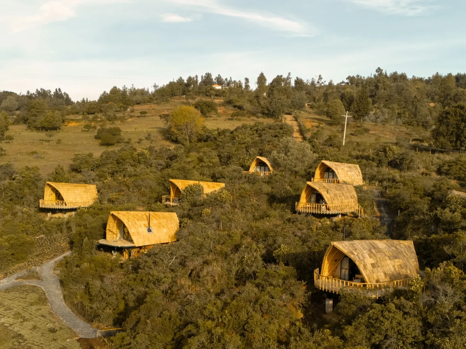 Cabinas de madera junto a un camino de piedra bajo cielo brillanterodeadas densos árboles verdes en colina Casa Selvaggio