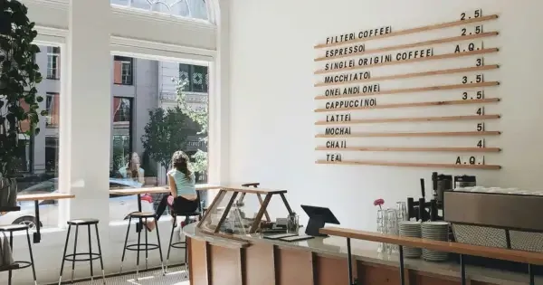 modern cafe with coffee sign behind counter and woman sitting down in front of window