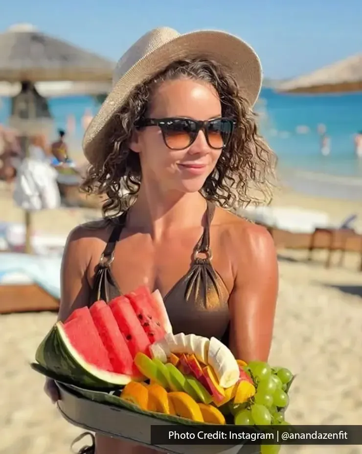 A woman holding a cut-fruit tray, posing for a picture on the beach - Lexis MY