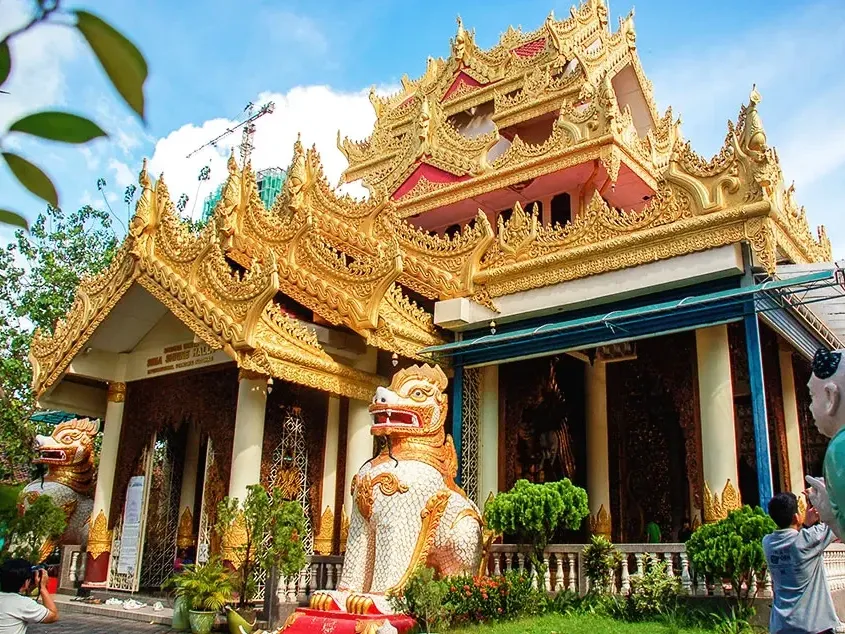 A golden burmese temple featuring intricate statues and a prominent lion statue at the entrance - Lexis Suites Penang