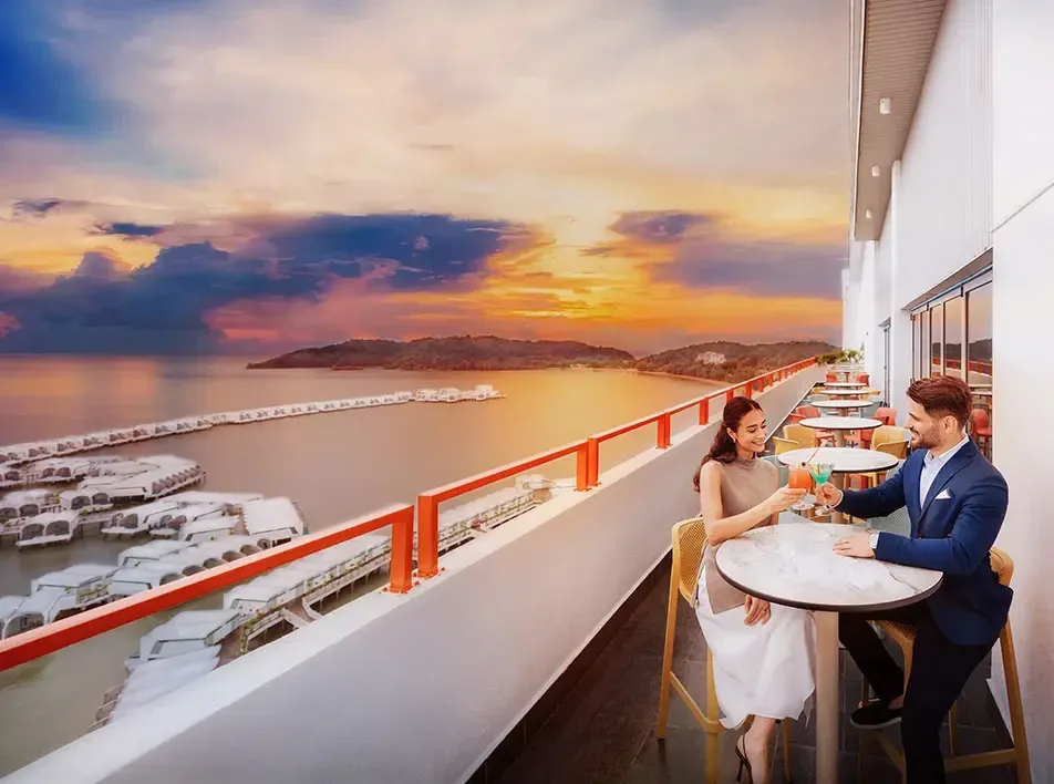 A couple sitting at a seaside club, enjoying drinks together - Lexis MY