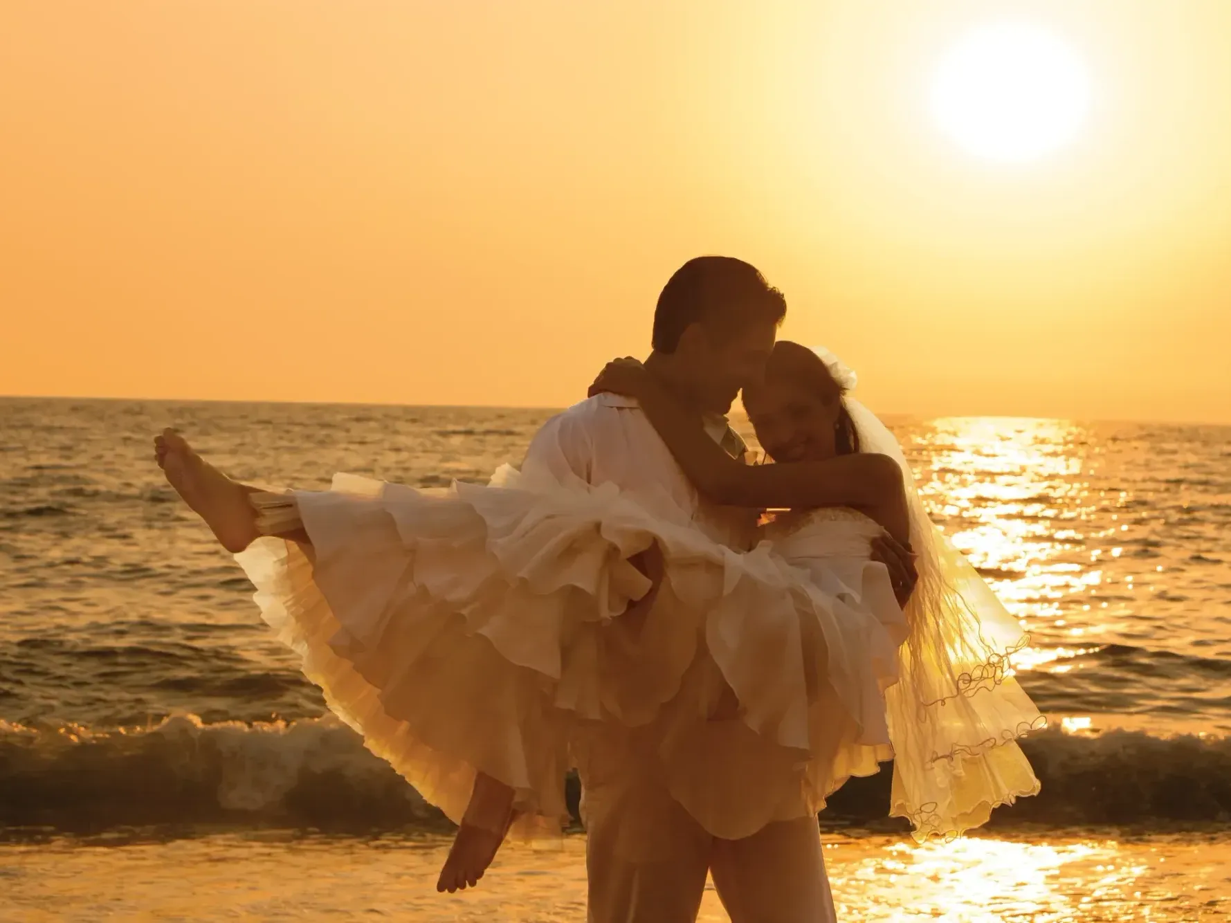 Groom lovingly carrying his bride on glowing beach at Saint Martin Beach Resort & Spa, featuring St. Martin vacation packages