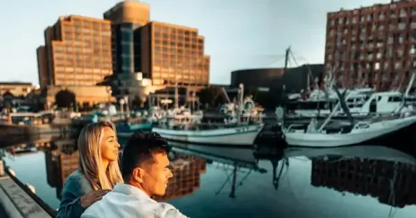 Couple sitting by the waterfront at sunrise, facing the harbour with boats and Hotel Grand Chancellor Hobart in background 