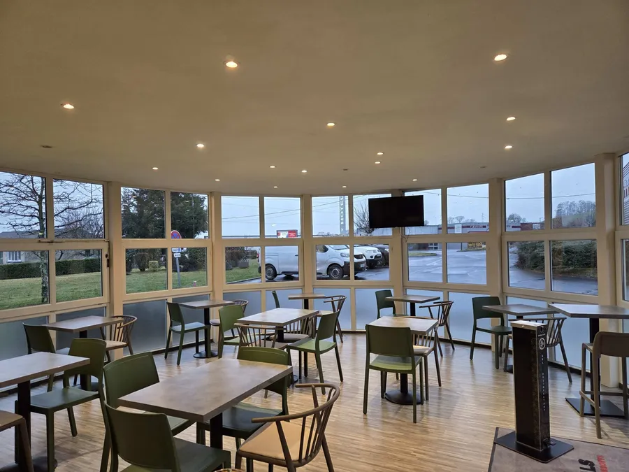 Tables et chaises dans un restaurant moderne avec vue sur parking au Hôtel Aurillac Aéroport.