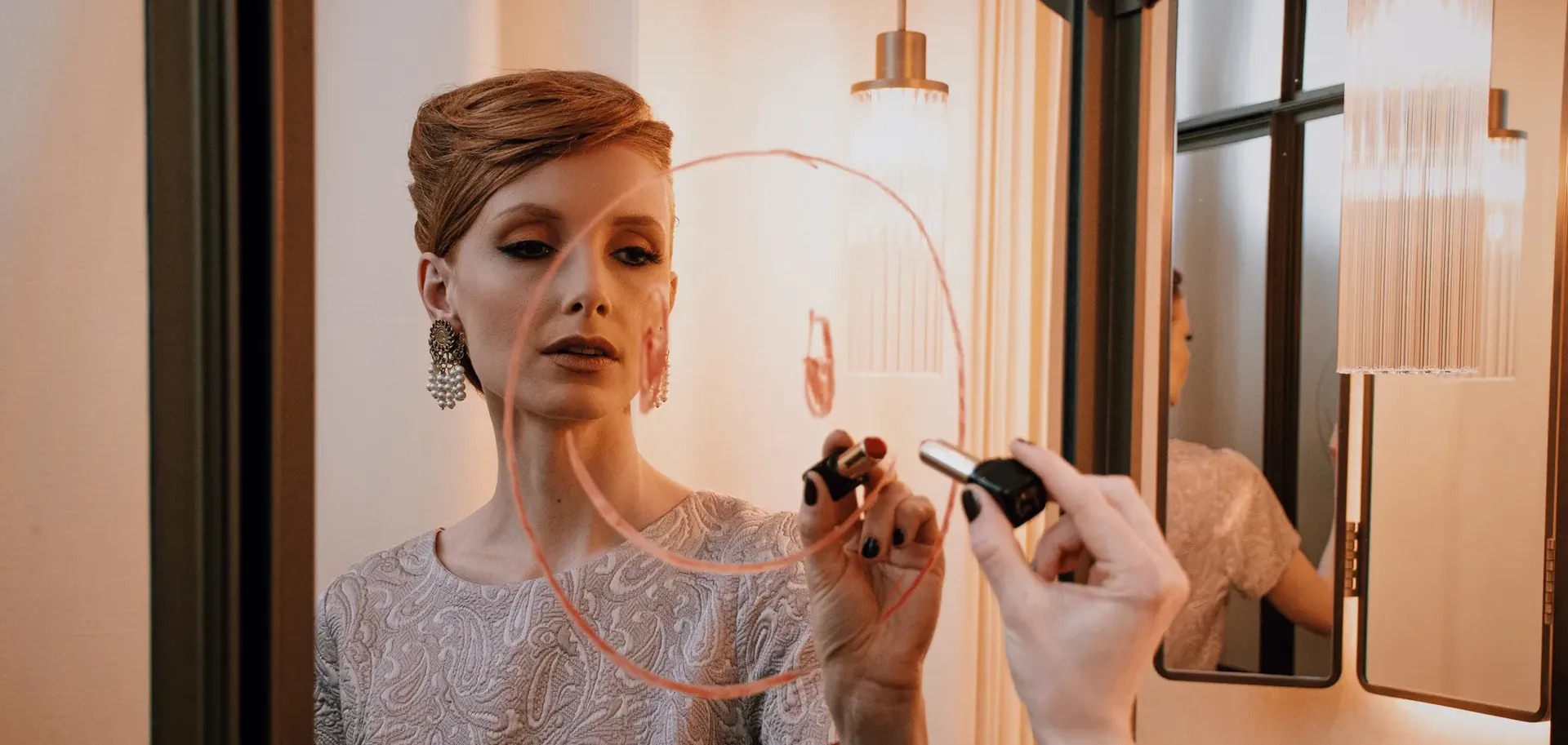 Woman in elegant lace dress applying makeup with mirror in modern bathroom with warm lighting in Hotel Motto