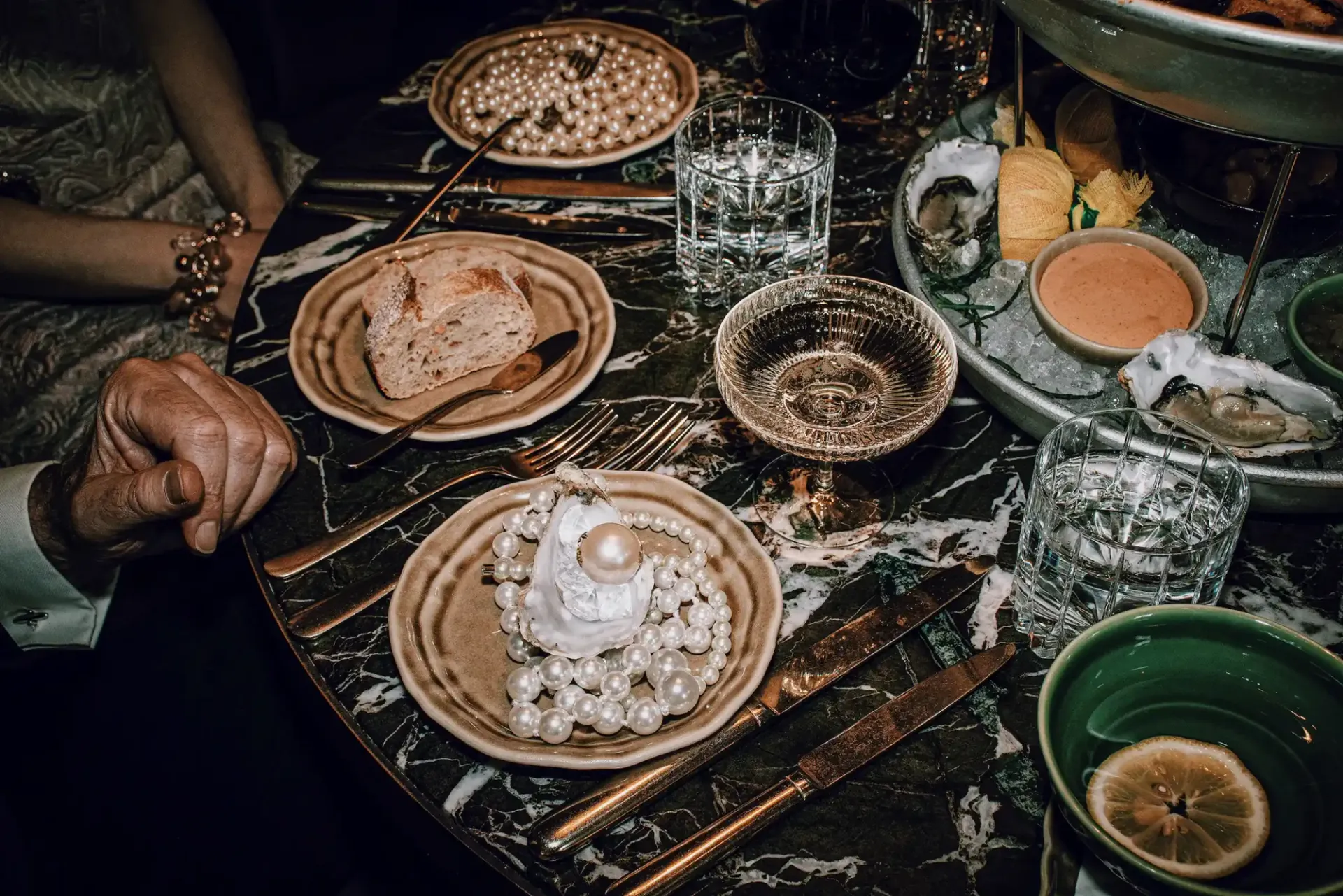 Elegante Tischdekoration mit Kristallgläsern, Perlen und Austern auf Marmortisch im Hotel Motto