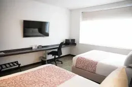 Two double beds facing e a long dark work desk with a black office chair under a wall-mounted TV inside Hotel B3 Virrey