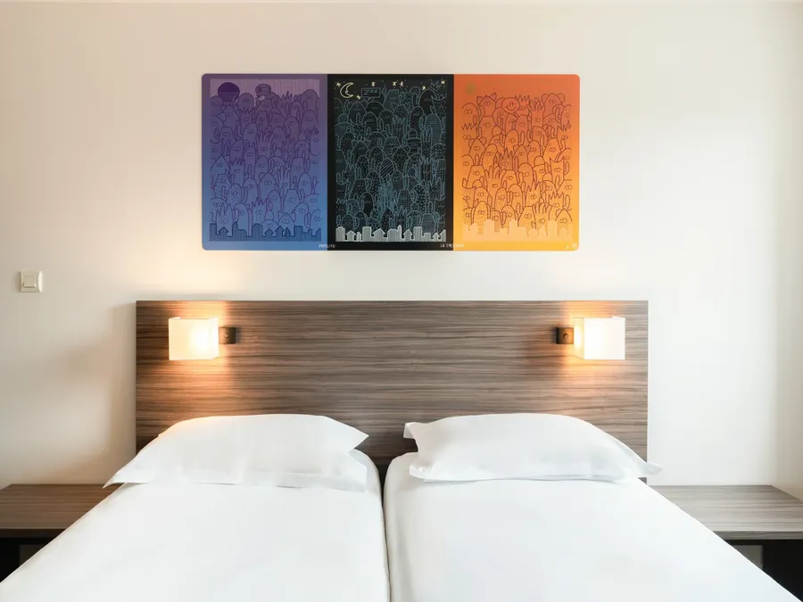 Two twin beds with white linens and artwork above at Appart’Hôtel Hévéa in Valence.