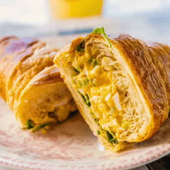 A croissant sandwich cut in half on a floral plate, with a yellow drink in the background.
