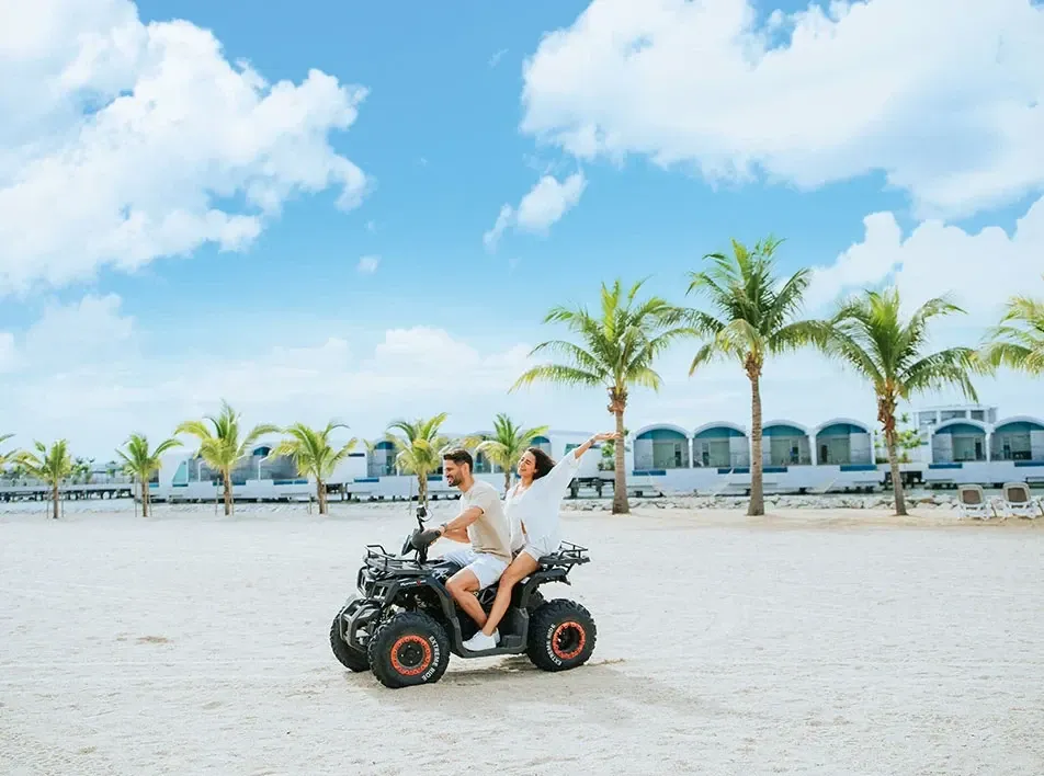 Couple riding an ATV together on a sandy beach.