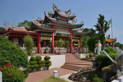 A serene Chinese temple beside a tranquil pond and a detailed statue surrounded by lush greenery