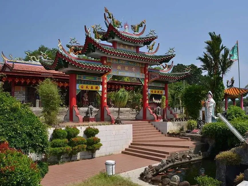 A serene Chinese temple beside a tranquil pond and a detailed statue surrounded by lush greenery - Lexis Port Dickson