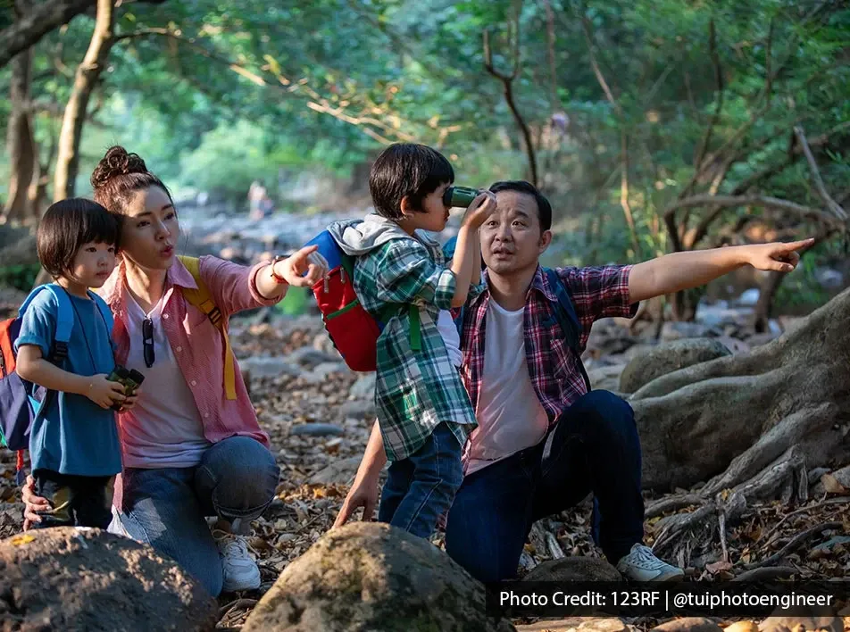 Parents and children hiking through a wooded area during an outdoor adventure.