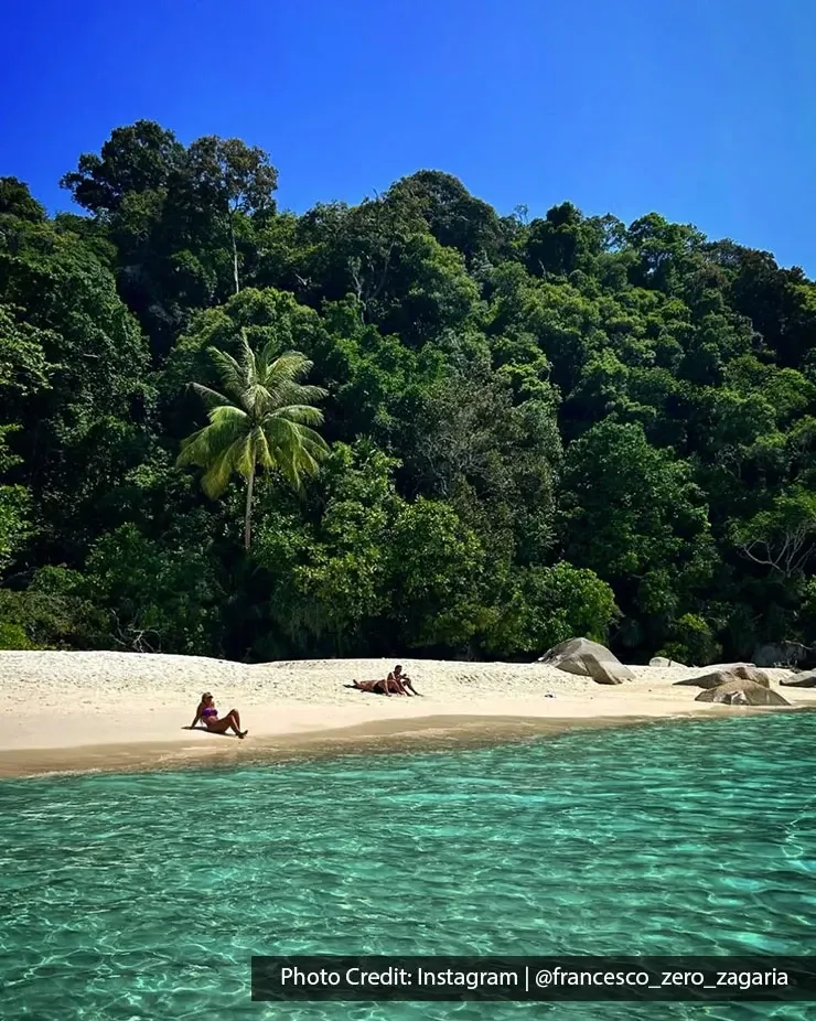 Tropical beach at Pulau Perhentian Besar surrounded by lush forest.