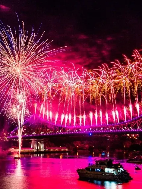 Fireworks over a city bridge at night with boats in the water during Riverfire 2026.