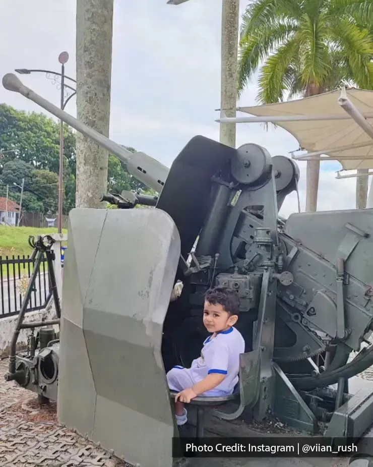 A child was sitting on a historical military anti-aircraft gun display at Port Dickson's Army Museum - Grand Lexis Port Dickson