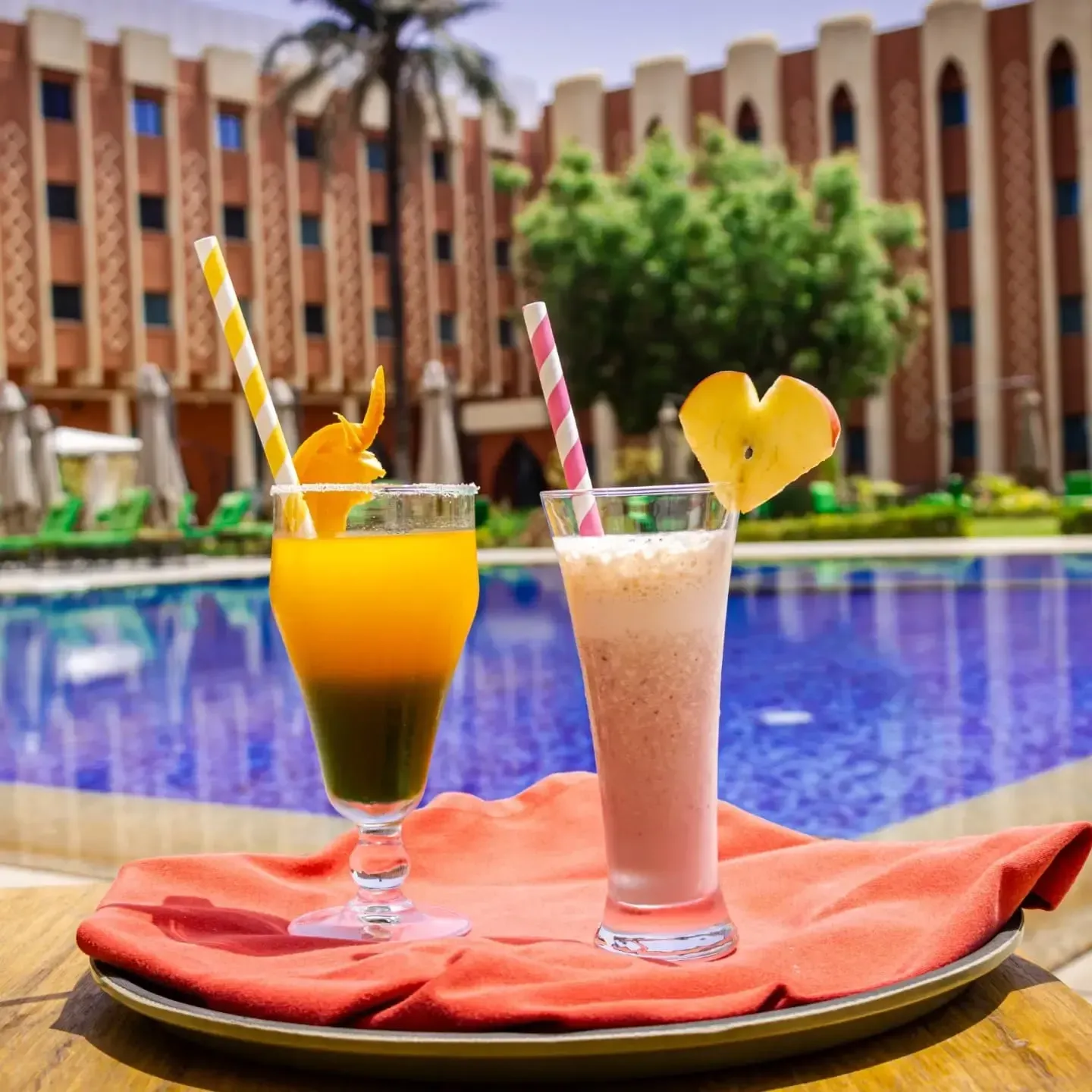 Deux verres de smoothies décorés avec des pailles et des fruits devant la piscine.de l'hôtel azalai ougadougou