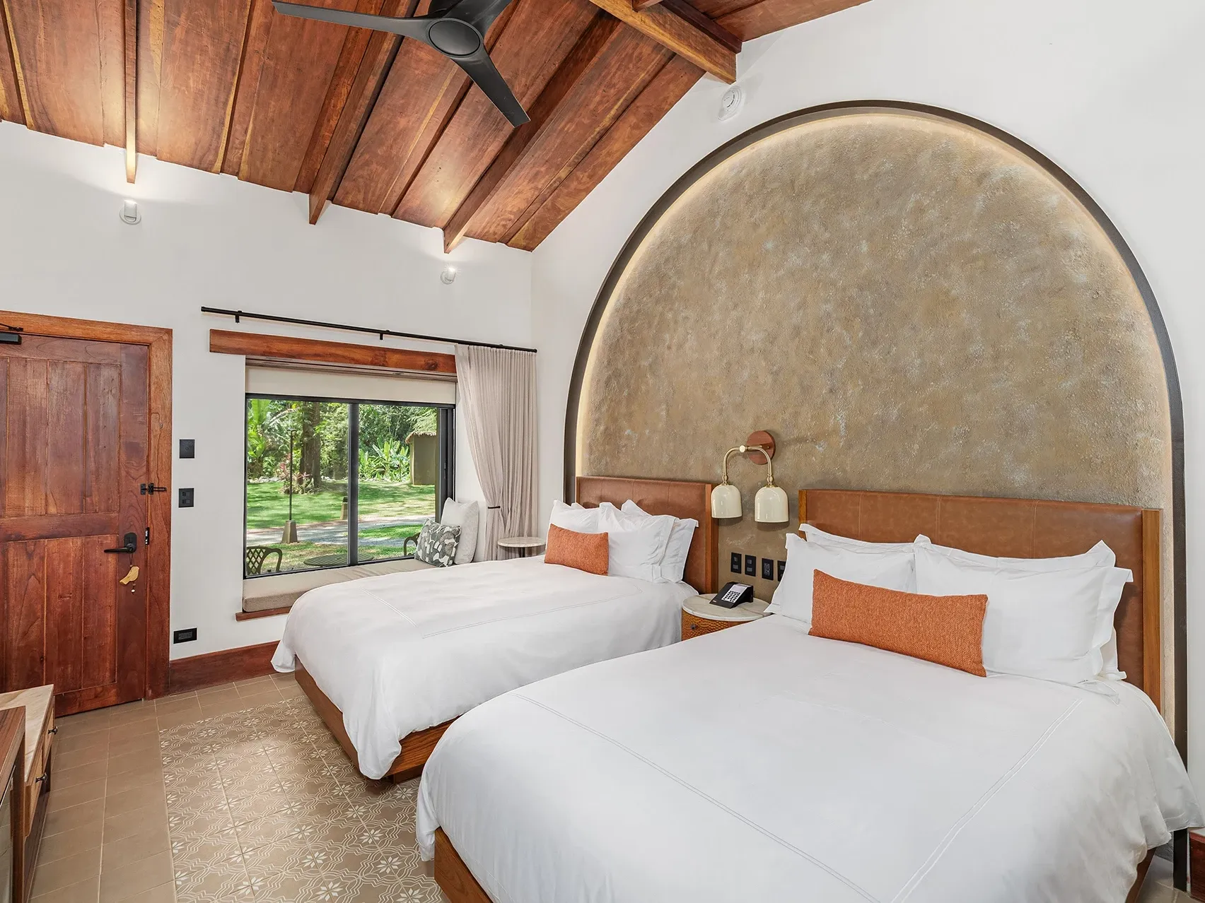Habitación doble de lujo con una cama junto a la pared texturizada y un banco junto a la ventana en Santa Lucía Jungle Hacienda, un complejo turístico situado en la selva tropical de Costa Rica