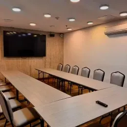 Sala de conferencias con mesas de madera en forma de U frente a una pantalla de pared en Unika Hotels