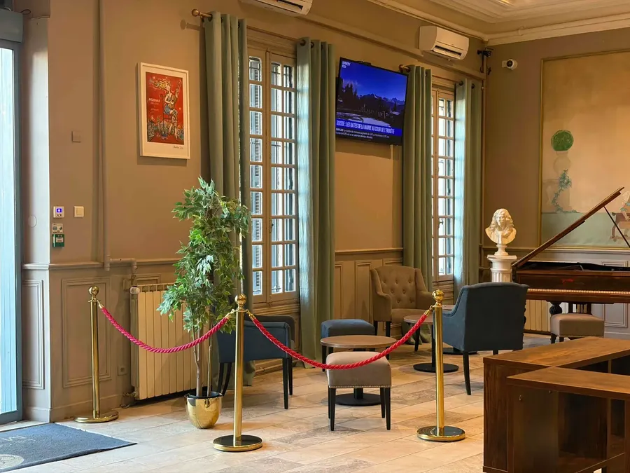Salle d'attente élégante avec fauteuils, TV, plante et piano au Grand Hôtel Molière