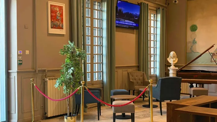 Salle d'attente élégante avec fauteuils, TV, plante et piano au Grand Hôtel Molière