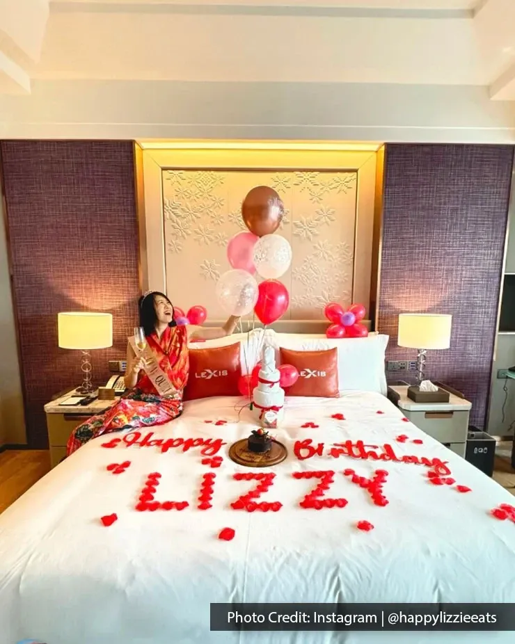 A woman on bed surrounded by colourful balloons and a cheerful birthday message.