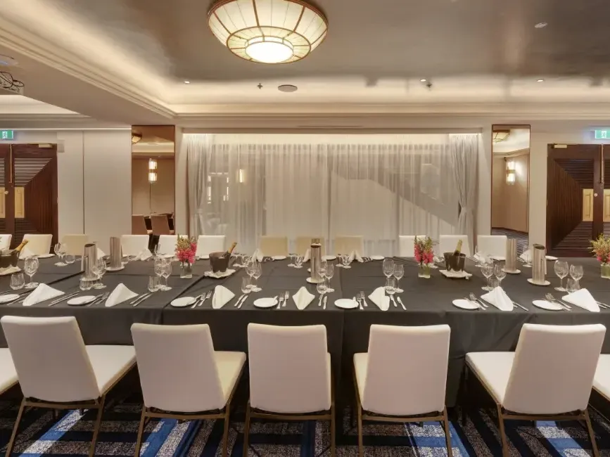 Elegant banquet room with long table set for formal dining, featuring white chairs and pink floral centerpieces.