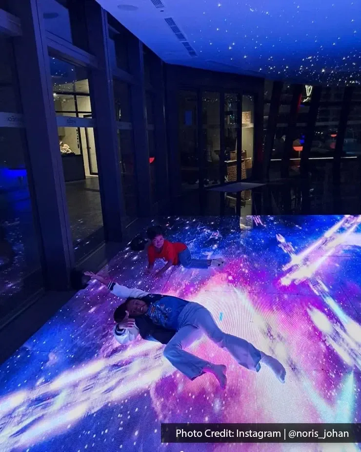 Kids lying on a galaxy-themed floor, surrounded by stars and cosmic designs in a cosy room.